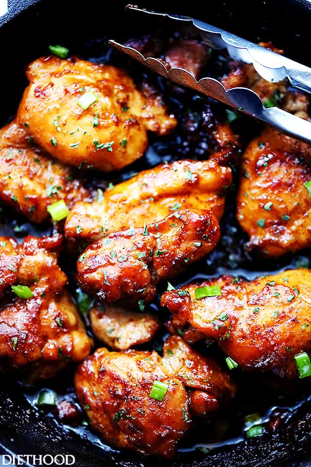 Overhead view of cooked sweet and sticky chicken thighs, brushed with a sauce and garnished with green onions.