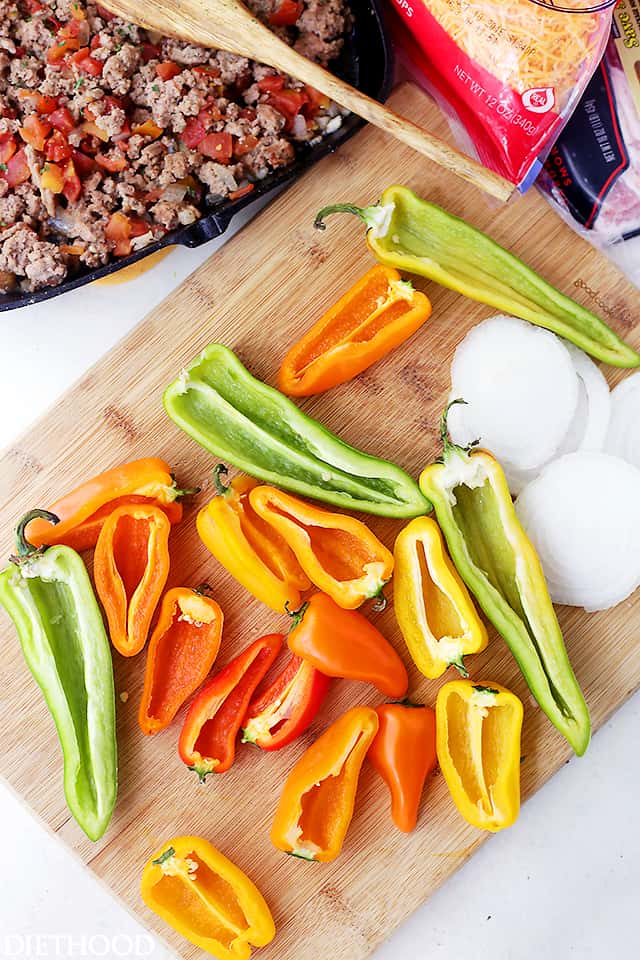 Overhead view of mini sweet peppers sliced in half on a wooden cutting board.