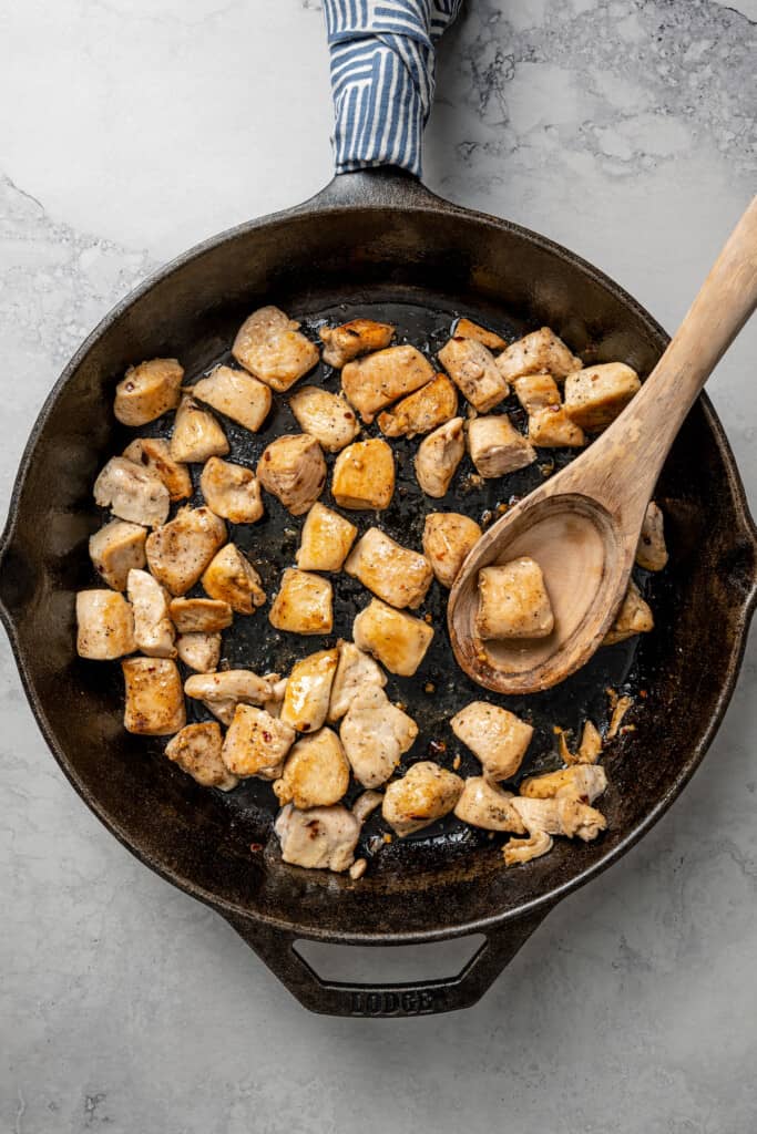 Chicken cooking in a skillet with a wooden spoon