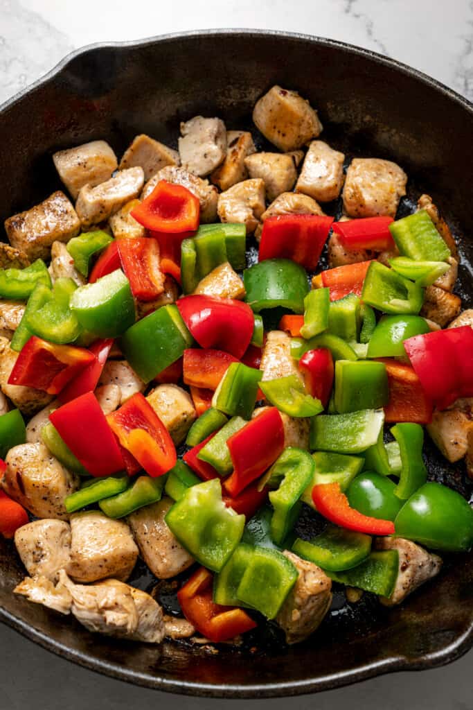 Raw bell peppers on top of cooked pieces of chicken in a skillet