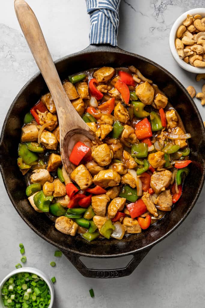 Overhead view of a skillet of cashew chicken with a wooden spoon