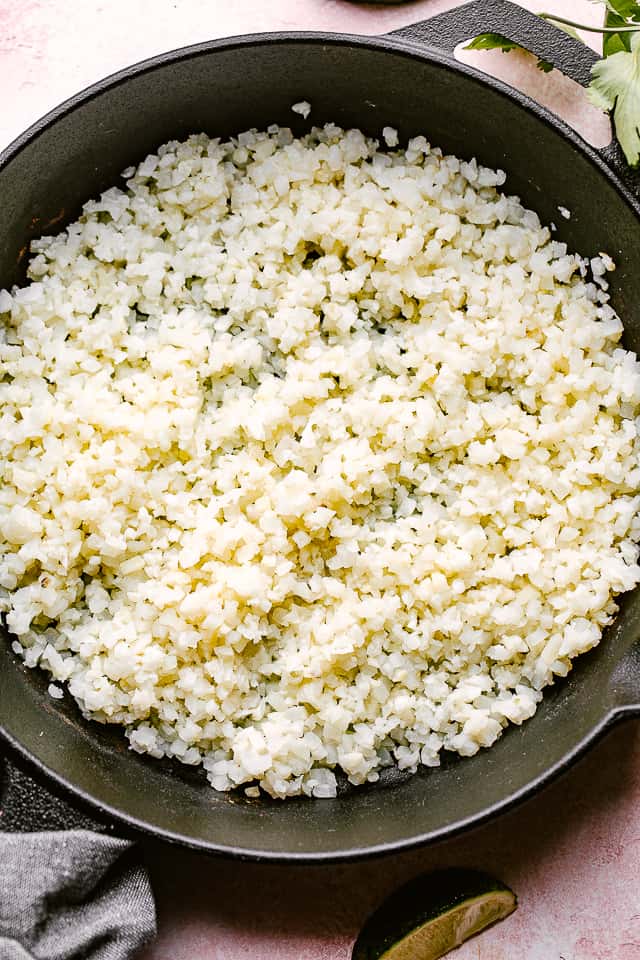 Cooking cauliflower rice in a dark skillet.