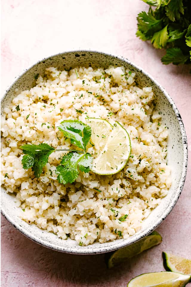 Coconut lime cauliflower rice served in a bowl and garnished with cilantro and lime.