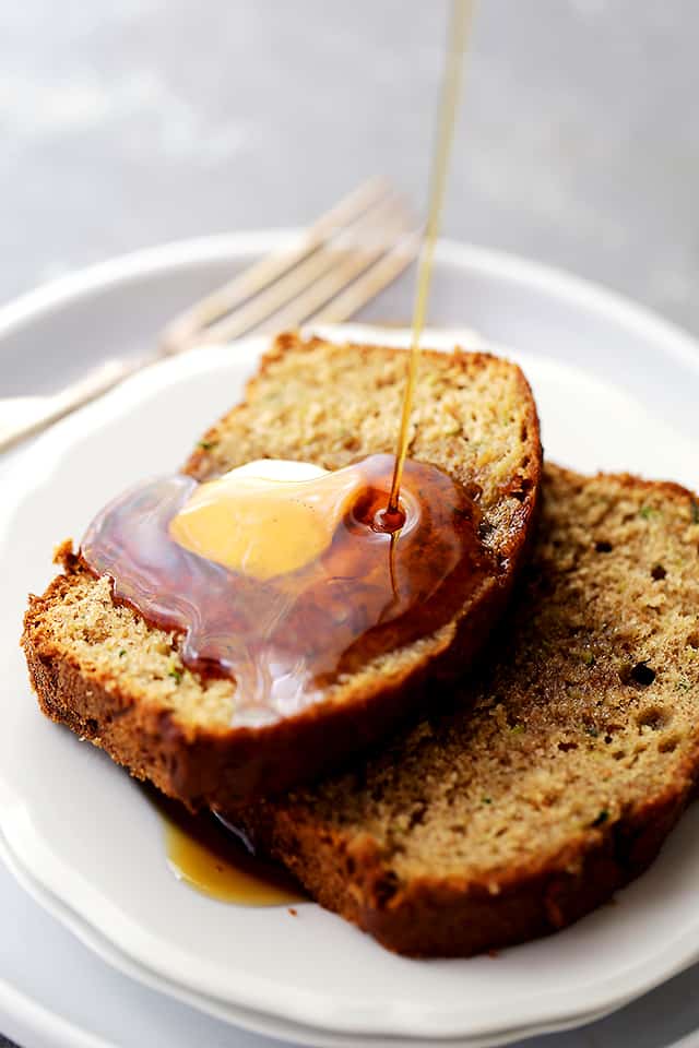 two slices of zucchini apple bread on a plate, with a drizzle of maple syrup pouring over it.