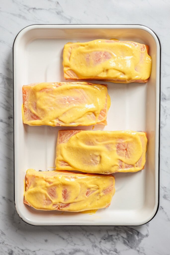 Four salmon fillets on a baking sheet coated with honey mustard sauce.