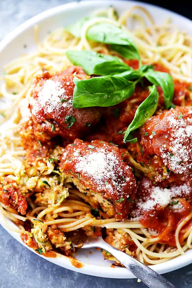 Zucchini Meatballs served on a dinner plate over some noodles and topped with tomato sauce and grated parmesan.