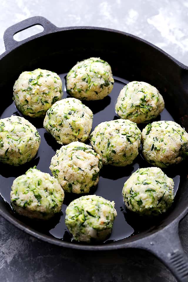 Cooking zucchini meatballs in a cast iron skillet.