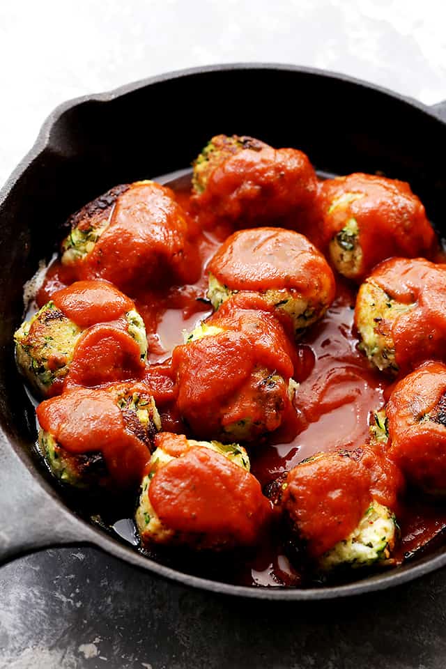 Zucchini meatballs are cooking in a cast iron skillet and in tomato sauce.