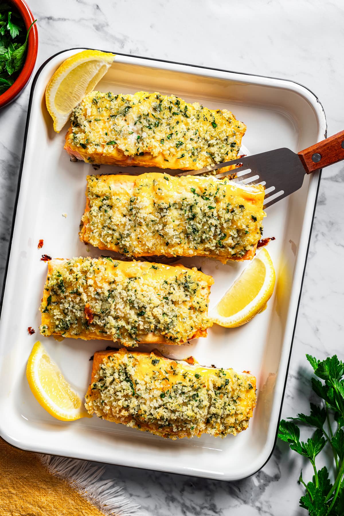 Baked honey mustard salmon fillets crusted with panko breadcrumbs on a baking sheet, with a spatula tucked under one fillet.