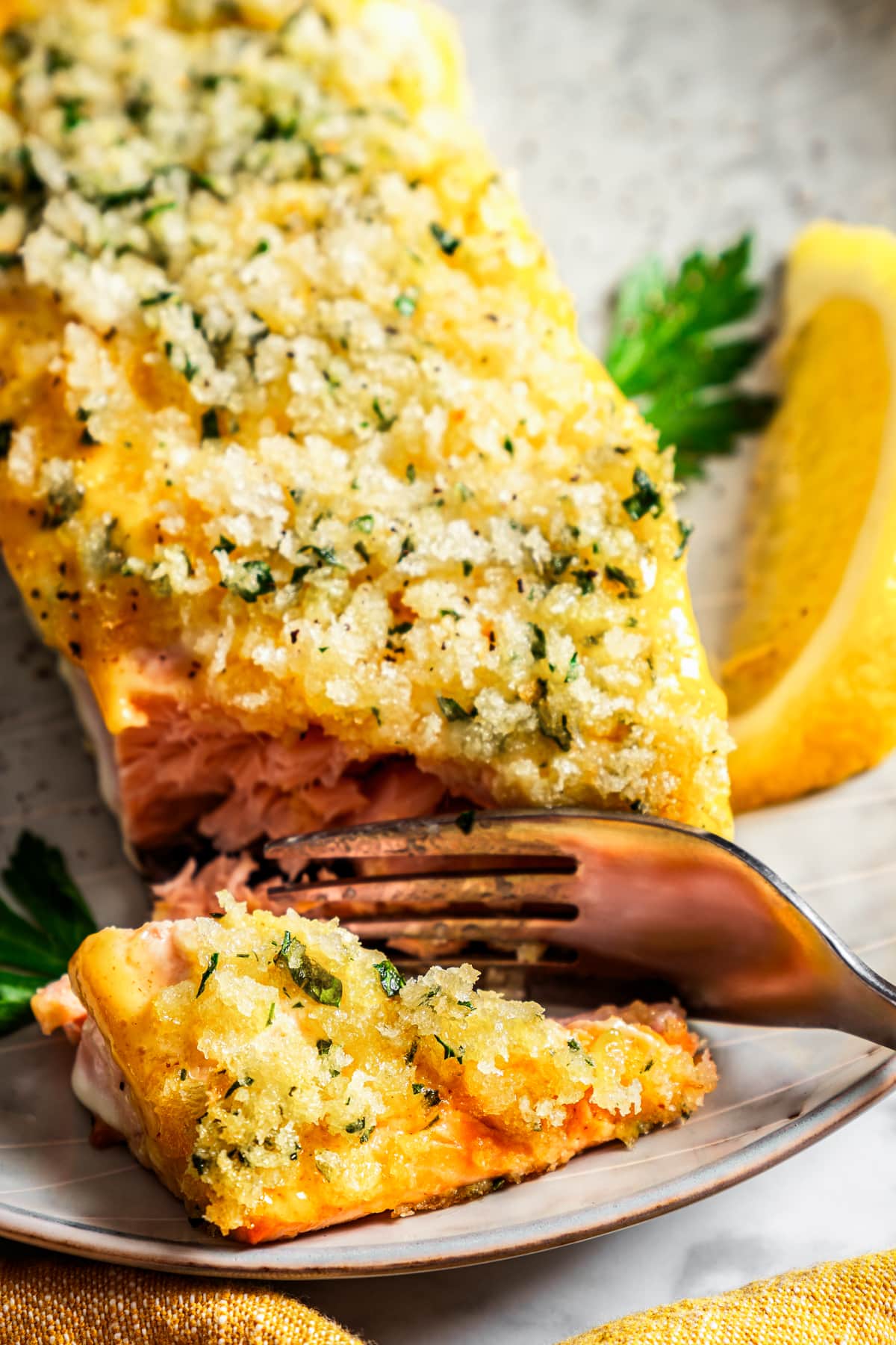 A fork cuts into the corner of a panko-crusted honey mustard salmon fillet on a plate next to a lemon wedge.