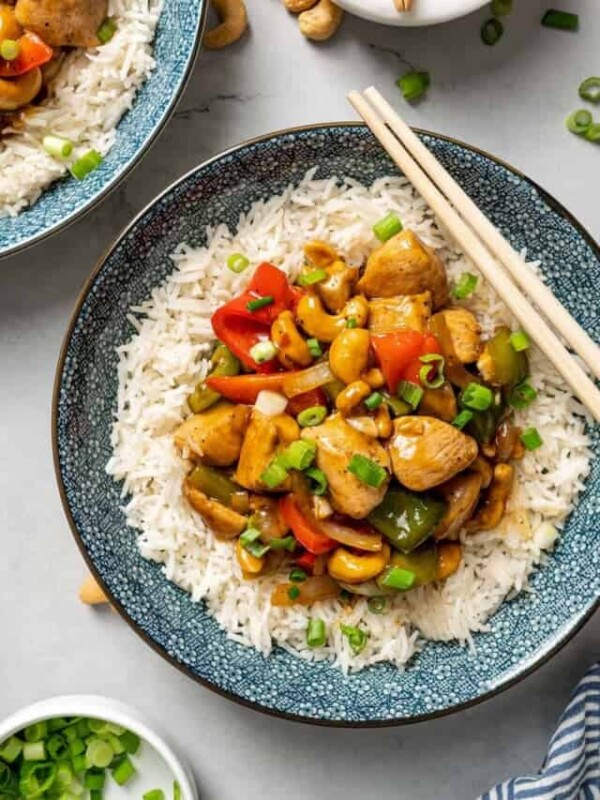 Overhead view of a plate of cashew chicken on rice with a pair of chopsticks, next to another plate