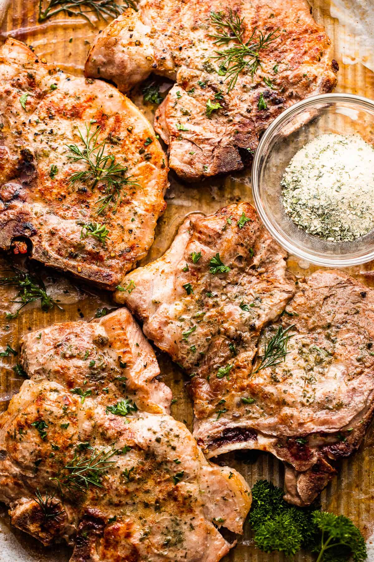 Tray with four baked pork chops and ranch seasoning in a small mixing bowl placed next to them.