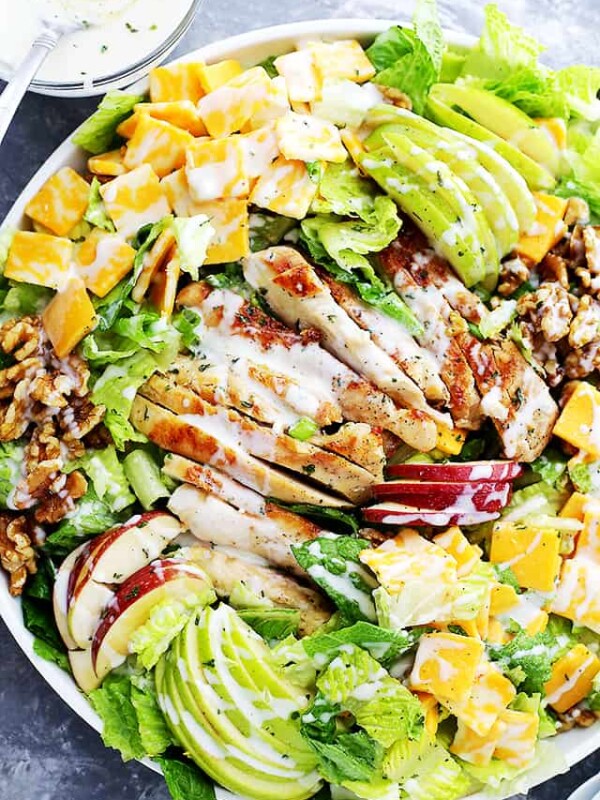 A large platter with salad greens, sliced apples, cubed cheddar cheese, walnuts, and drizzled with a creamy dressing.