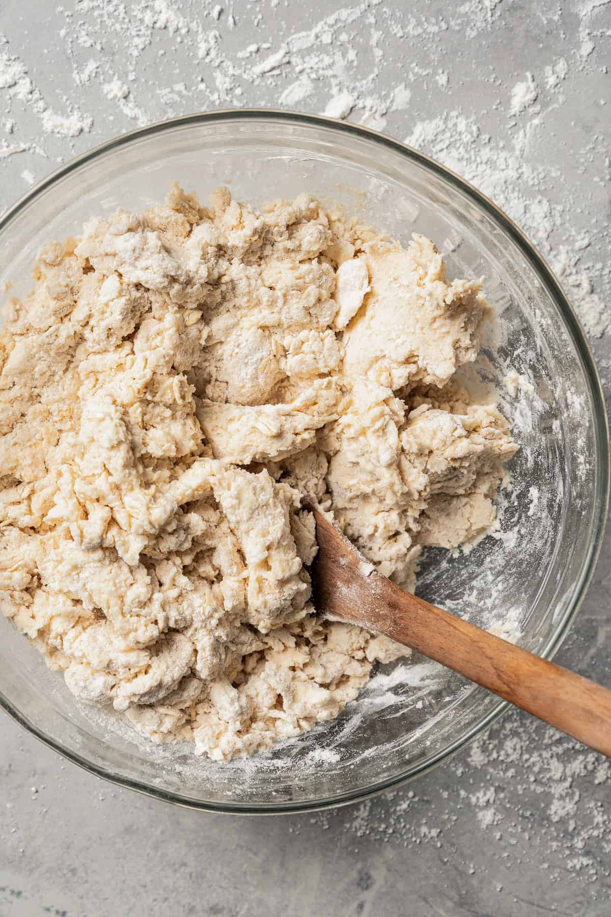 Cinnamon scone dough coming together in a glass mixing bowl with a wooden spoon.