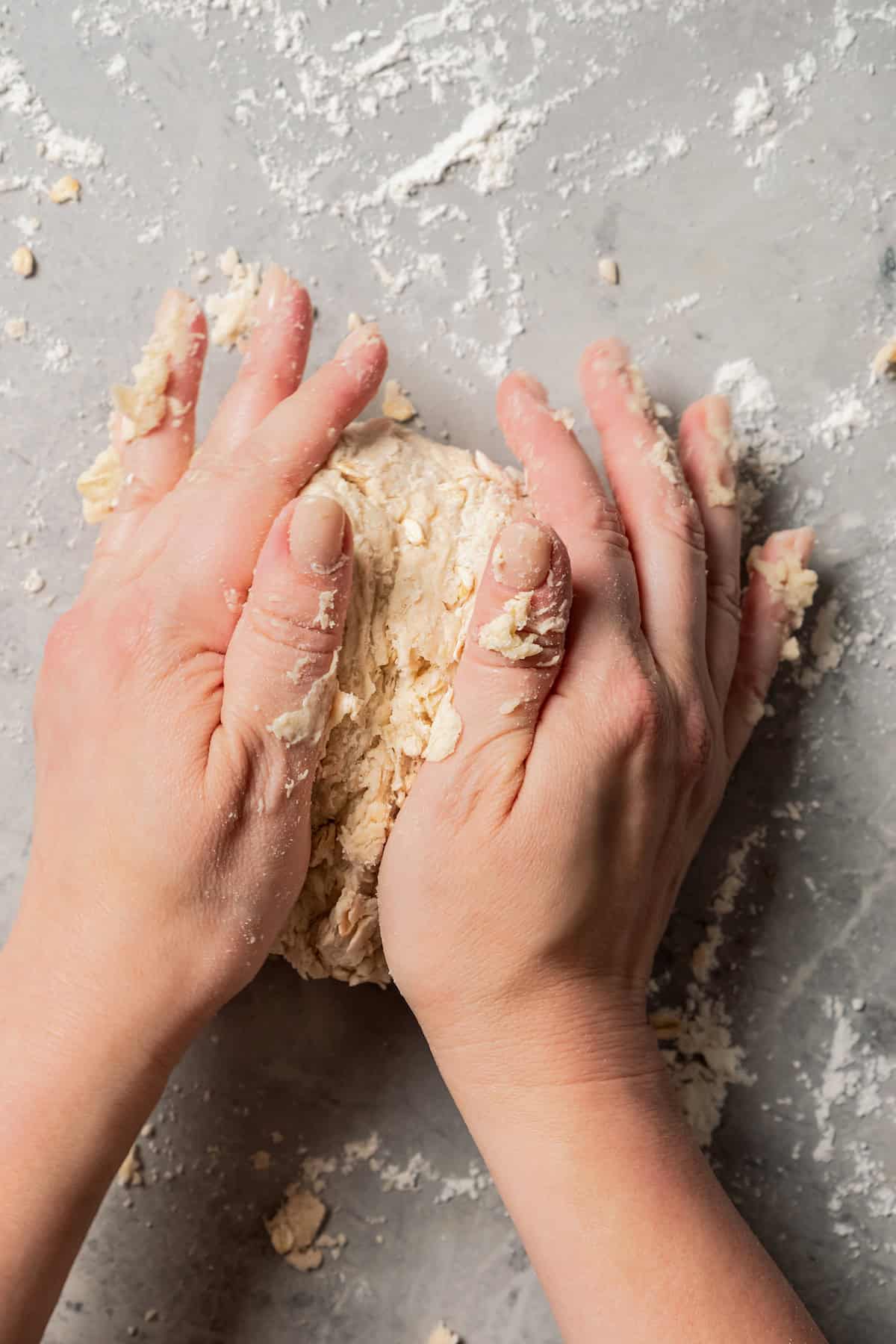 Two hands kneading scone dough on a floured countertop.