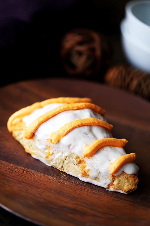 A pumpkin pie spice scone on a wooden plate, decorated with a cream glaze and icing drizzle.