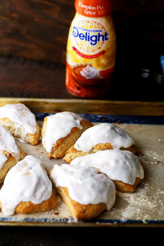 An assortment of glazed pumpkin spice scones on a baking sheet with a bottle of International Delight Pumpkin Pie Spice Creamer in the background.