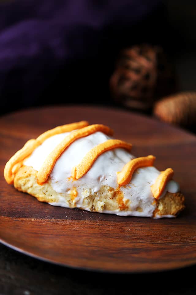 A pumpkin pie spice scone on a wooden plate, decorated with a cream glaze and icing drizzle.