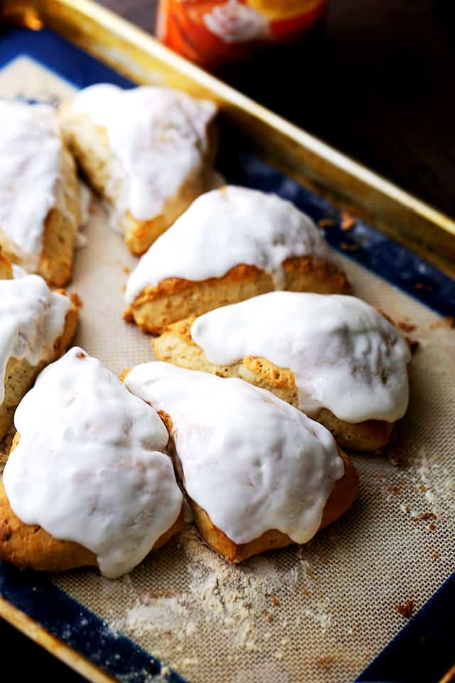 An assortment of glazed pumpkin spice scones on a baking sheet.