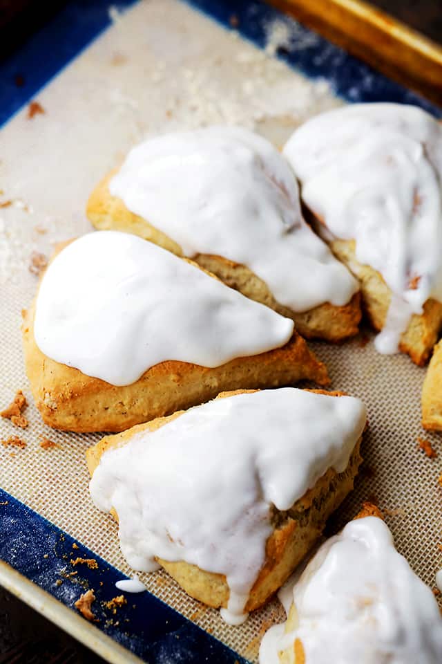 An assortment of glazed pumpkin spice scones on a baking sheet.