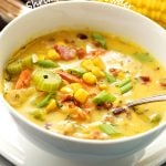 A white bowl filled with creamy chowder. Corn, shrimp, celery, and bacon are in the chowder.