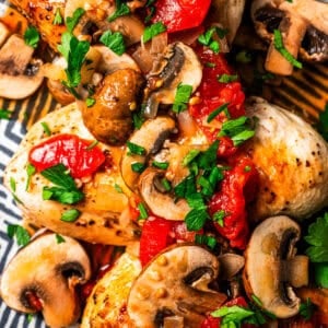 Close-up shot of chicken breasts topped with mushrooms, tomatoes, and fresh basil.