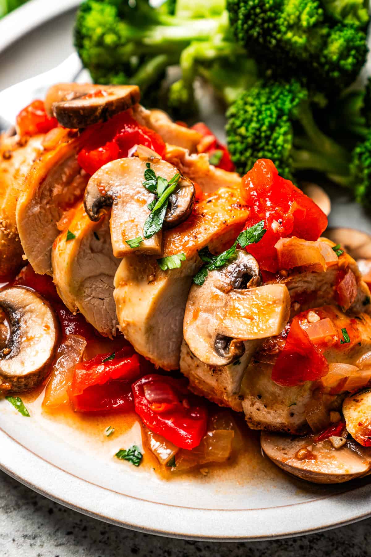 A serving of Chicken Marengo is cut into slices and is served next to a side of steamed broccoli on a plate.