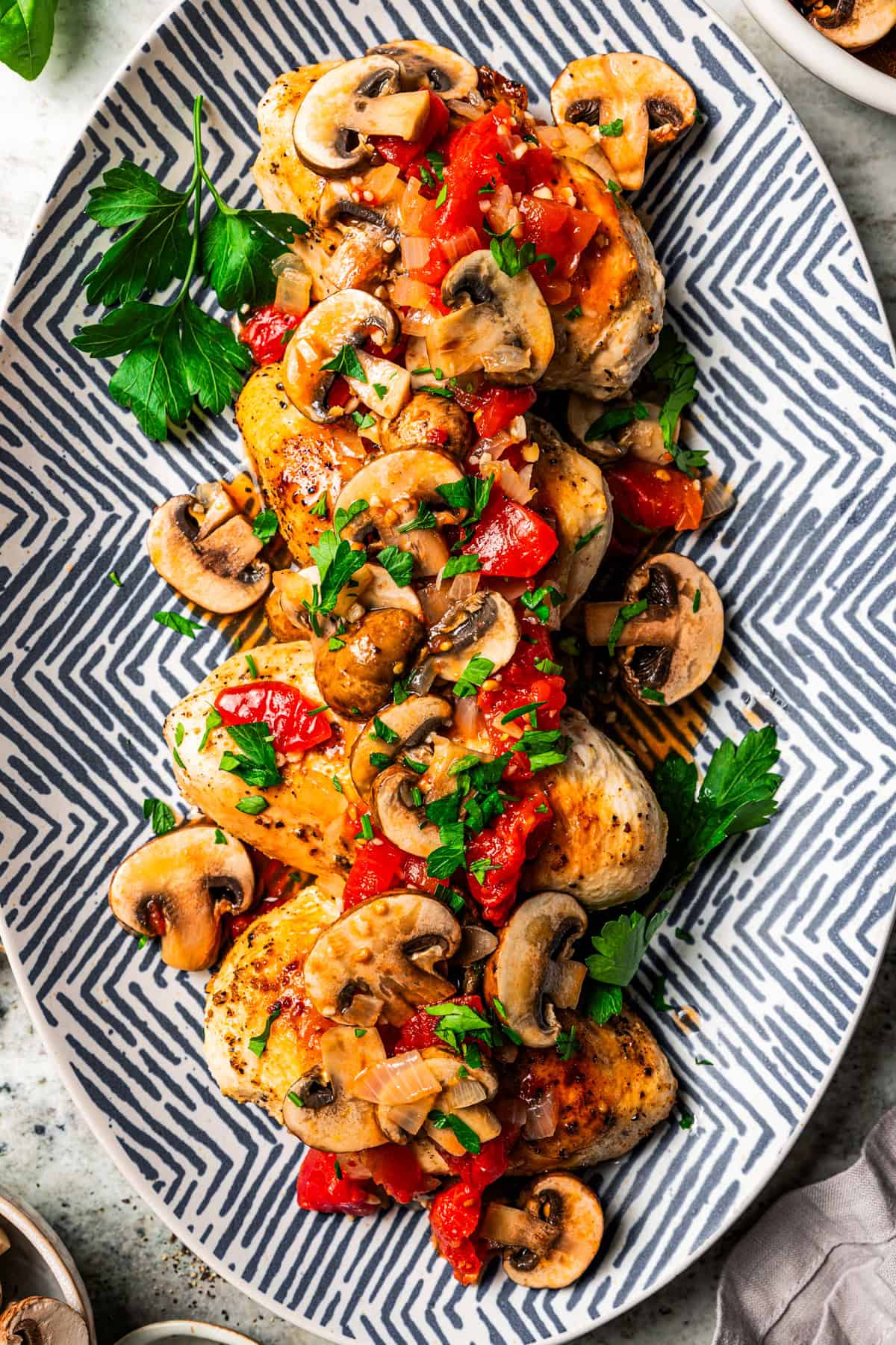 Cooked chicken breasts topped with tomatoes and mushroom sauce and served on an oval platter.