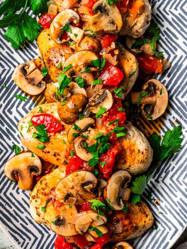 Four seasoned chicken breasts topped with tomato mushroom sauce and served on a patterned platter.