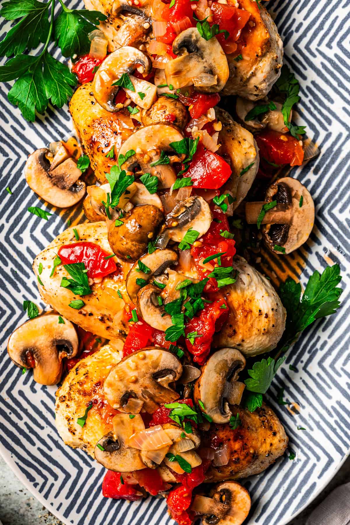 Four seasoned chicken breasts topped with tomato mushroom sauce and served on a patterned platter.