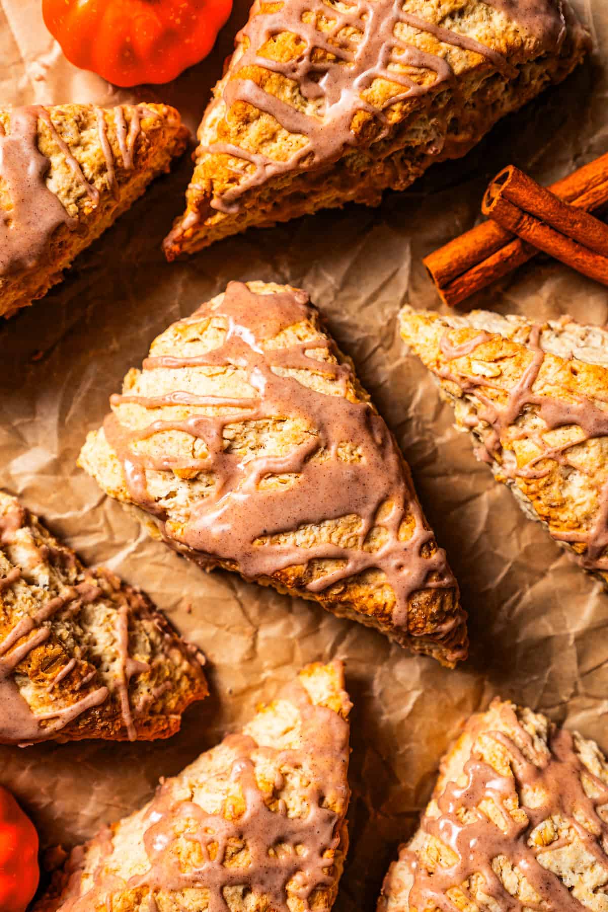 Glazed cinnamon scones arranged on a sheet of brown parchment paper, next to cinnamon sticks.