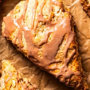 Overhead close-up of a glazed cinnamon scone set on a sheet of brown paper.