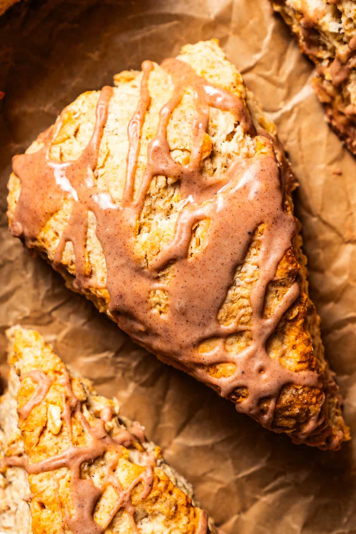 Overhead close-up of a glazed cinnamon scone set on a sheet of brown paper.