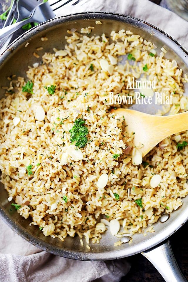 Almond Brown Rice Pilaf cooking in a skillet with a wooden spoon stirring through it.