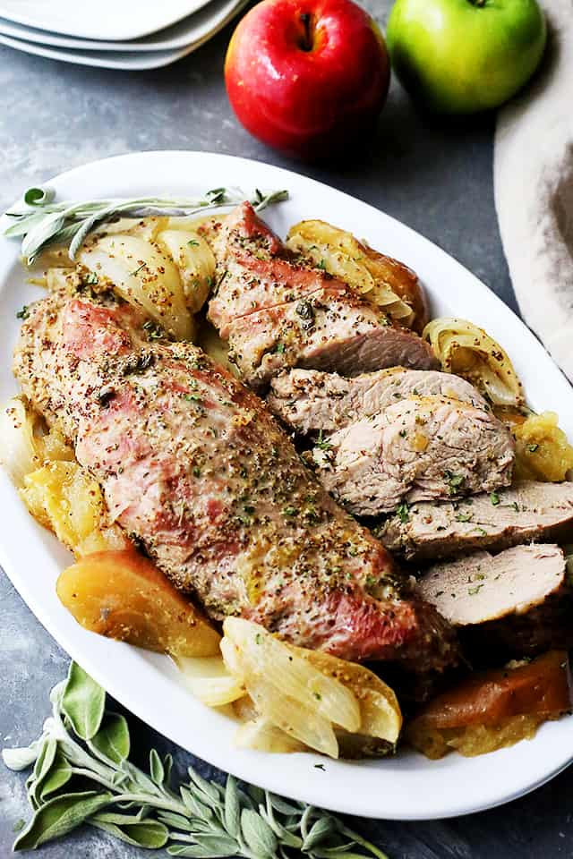 Partially sliced Apple Mustard Glazed Pork Tenderloin surrounded by baked apple and onion wedges on a serving platter