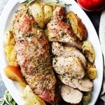 Baked pork on a serving plate beside two apples