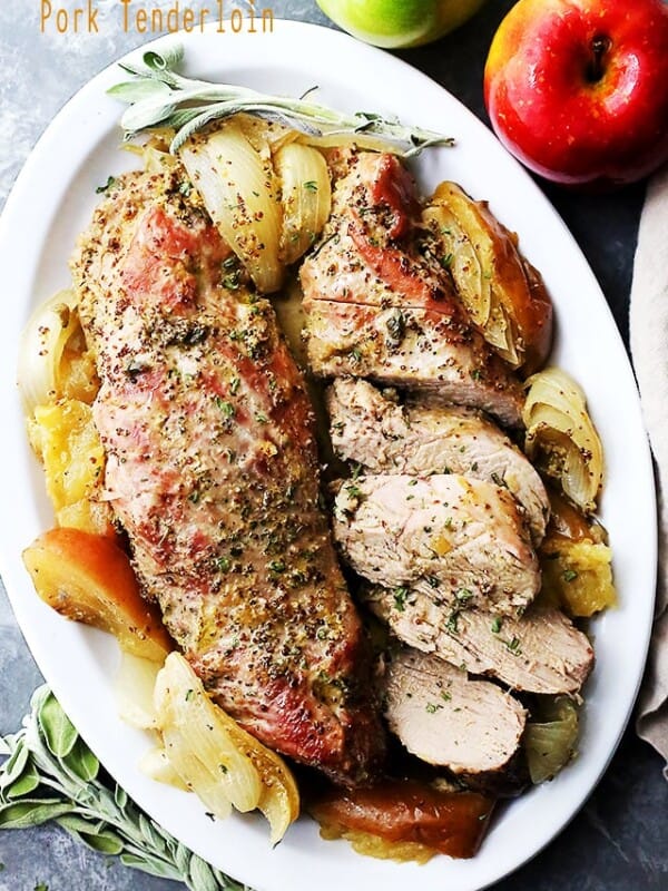 Baked pork on a serving plate beside two apples