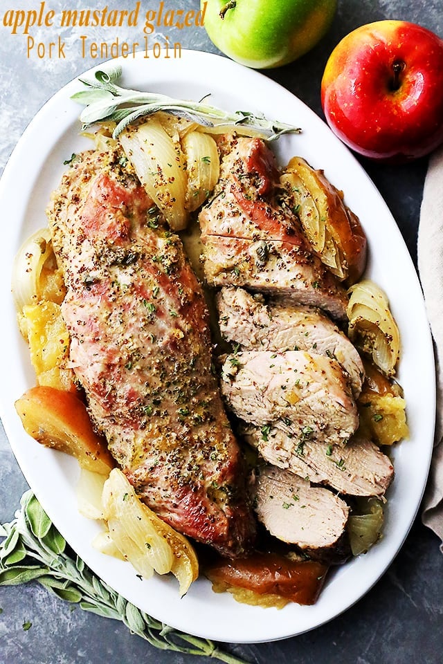 Baked pork on a serving plate beside two apples.