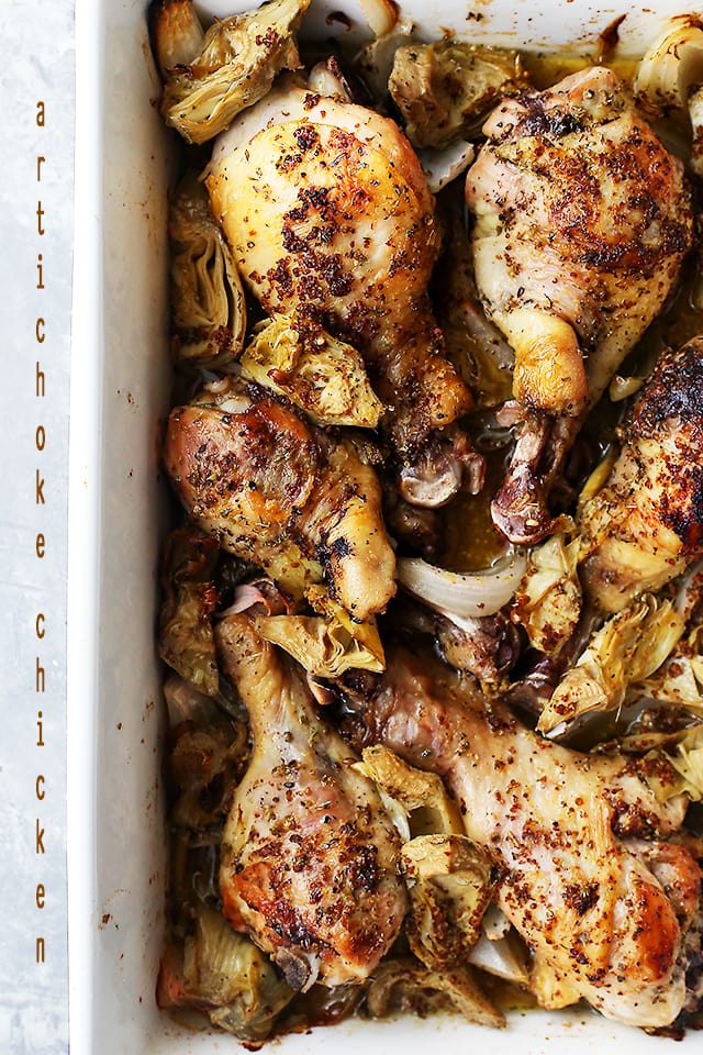 A white baking dish with cooked chicken drumsticks and artichoke hearts.