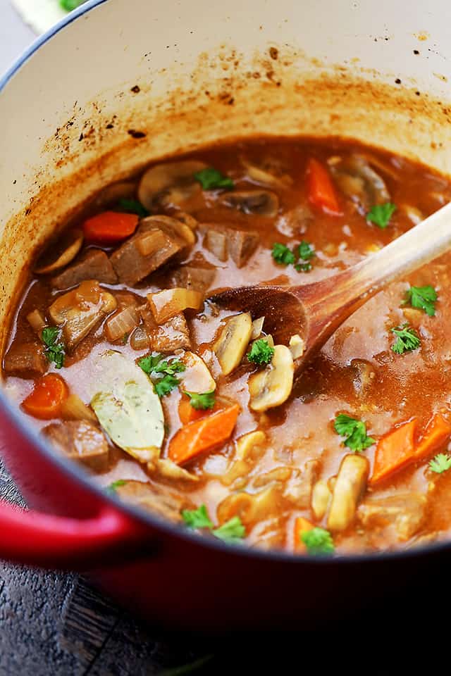 Beer Beef Stew cooking in a Dutch oven and a wooden spoon stirring through it.