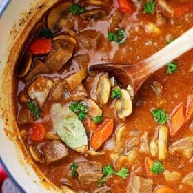 Overhead image of beef stew in a Dutch oven with a wooden spoon stirring through it.