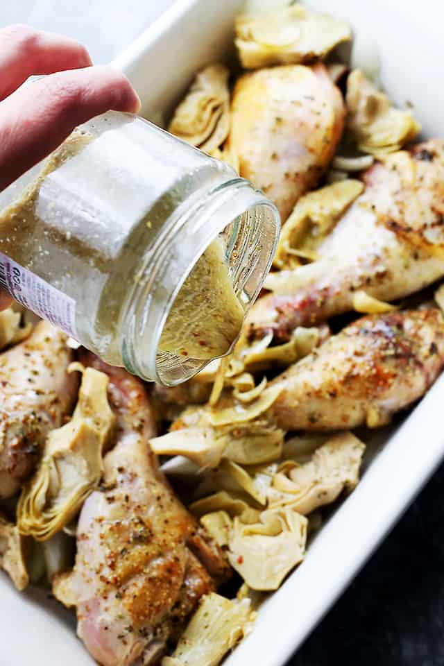 Pouring a marinade over chicken drumsticks and artichokes.