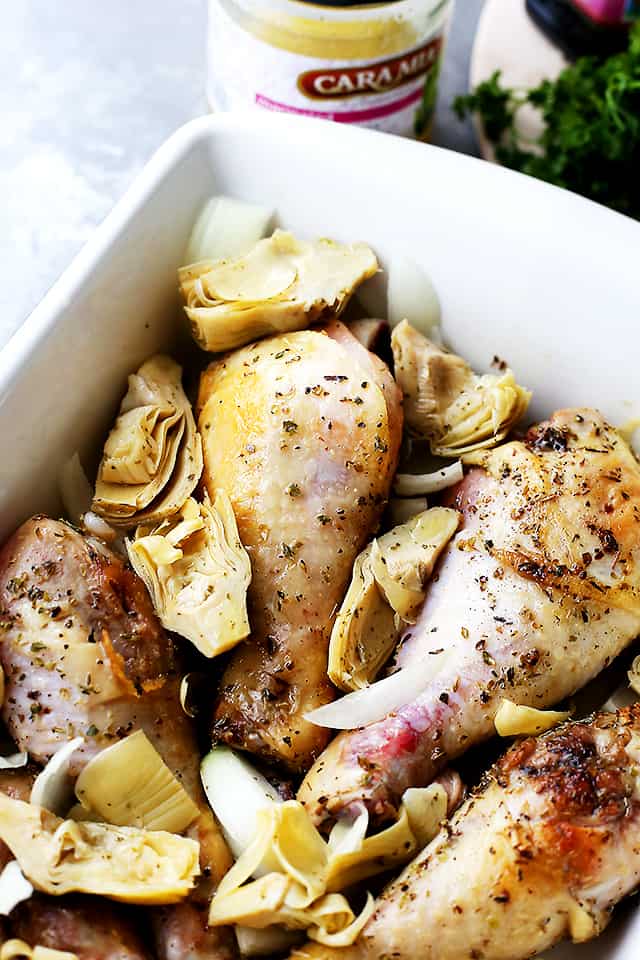 Chicken drumsticks with artichoke hearts in a white baking dish.