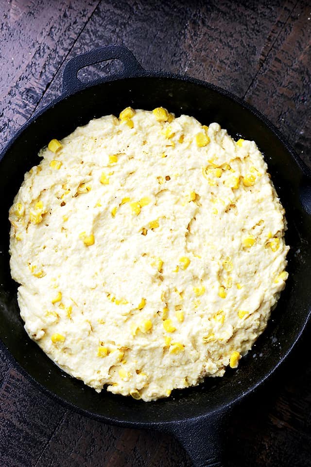 Cornmeal batter in a skillet with sweet corn and cheese, ready to be baked.