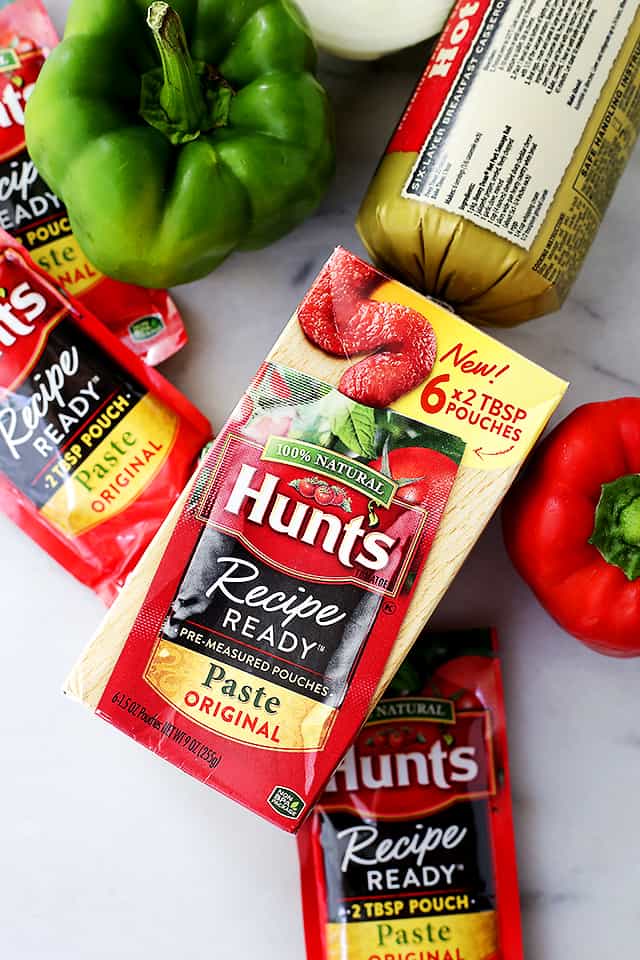 Photo of the ingredients for stuffed peppers, including tomato paste, hot pork sausage, and green and red bell peppers.