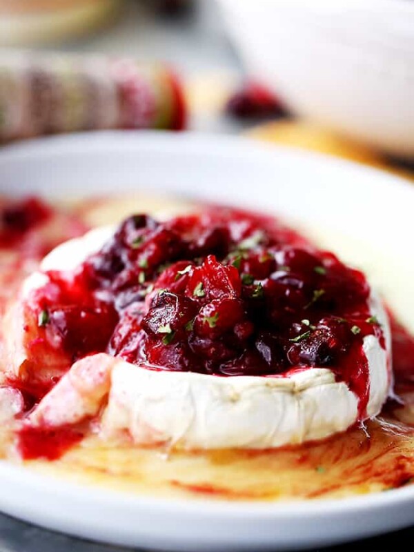 A wheel of melted baked brie cheese topped with red cranberry sauce.