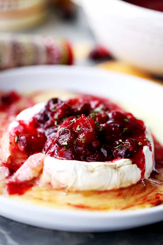 A wheel of melted baked brie cheese topped with red cranberry sauce.