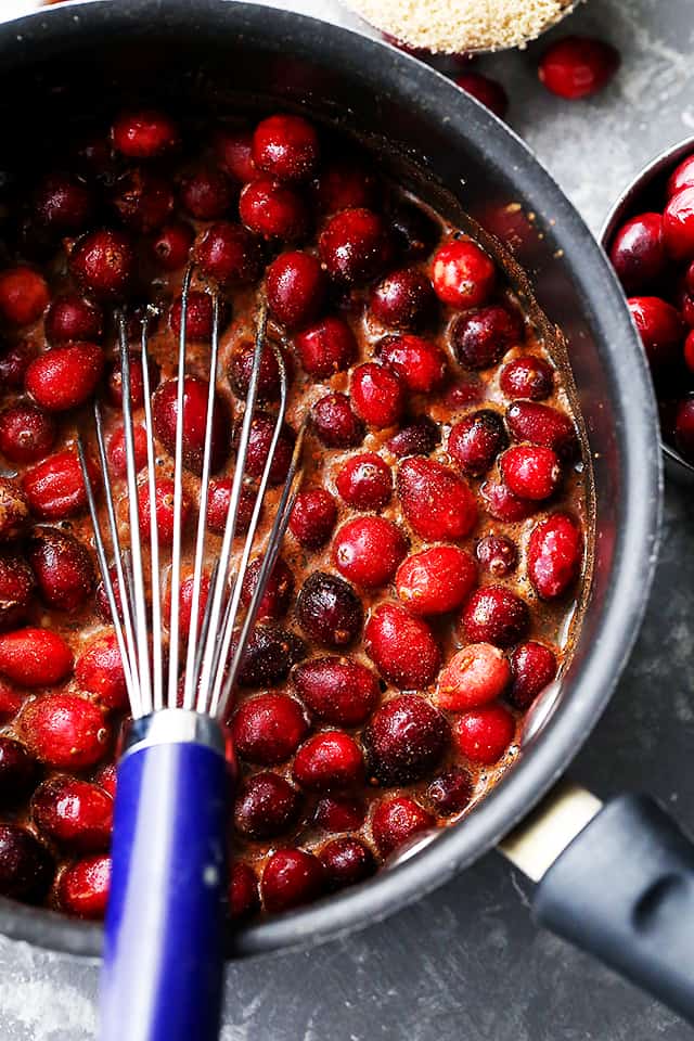 Cooked cranberries being stirred with a whisk.