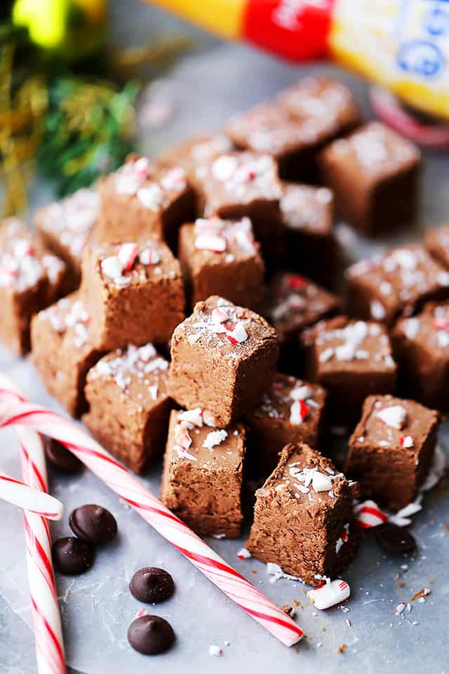 Squares of fudge stacked up and set next to candy canes.