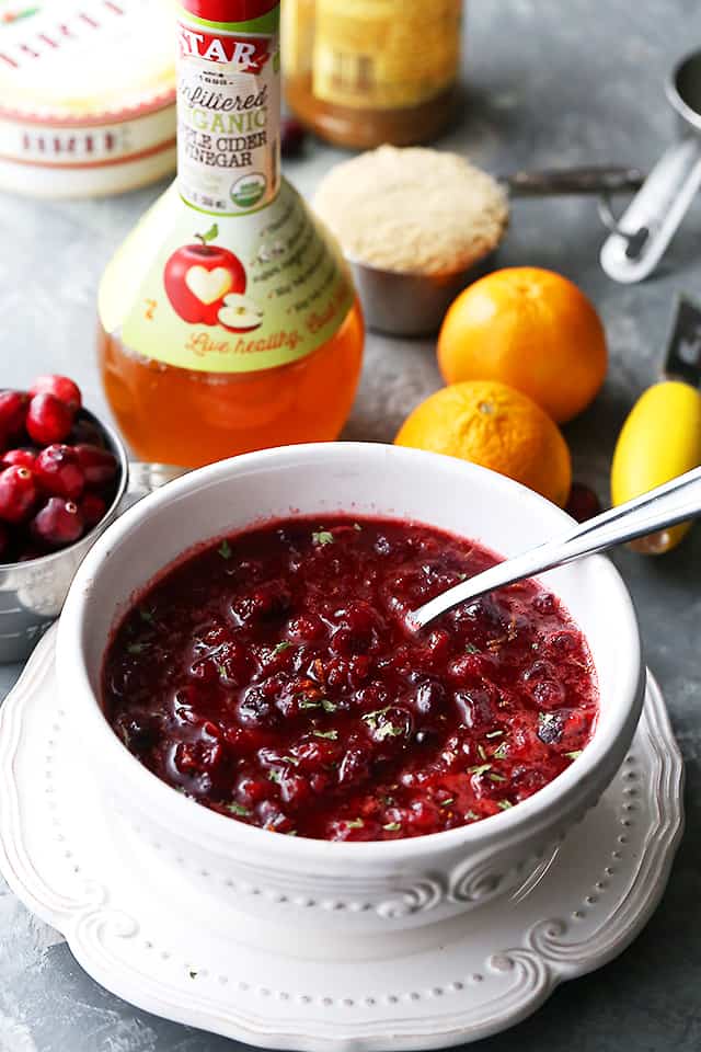 Spiced Cranberry Sauce in a serving dish with a spoon, next to a bottle of apple cider vinegar.